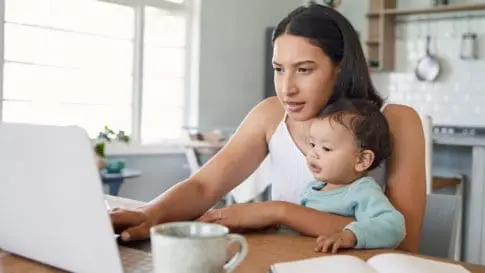 A mother works from home while holding her baby