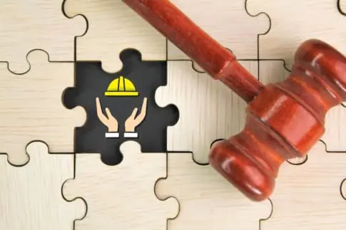 A gavel over a wooden puzzle with a construction hat represents labor law
