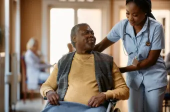 Older man in wheelchair talking to a nurse at nursing home