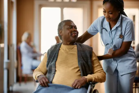 Older man in wheelchair talking to a nurse at nursing home