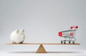 A seesaw balances a piggy bank and a grocery cart, representing the choice that households must make between spending and debt because of deteriorating household finances.