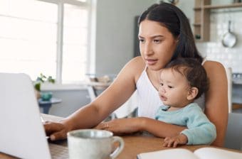 A mother works from home while holding her baby