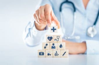 A medical professional stacks blocks that symbolize parts of the health care system