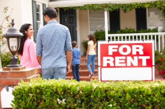 A family enters a rental house with a "For Rent" sign