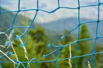 A blue net with a hole in it, with trees and mountains in the background // A hole in a net representing a gap in the safety net for working-age adults without dependents or disabilities