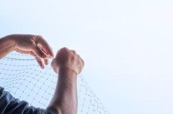 A pair of hands repairing a net, with a blue sky in the background
