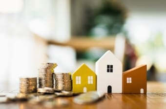 Stacks of coins next to wooden houses represent a fall in mortgage rates